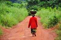Woman walking on dirt road with basket of crops on her head