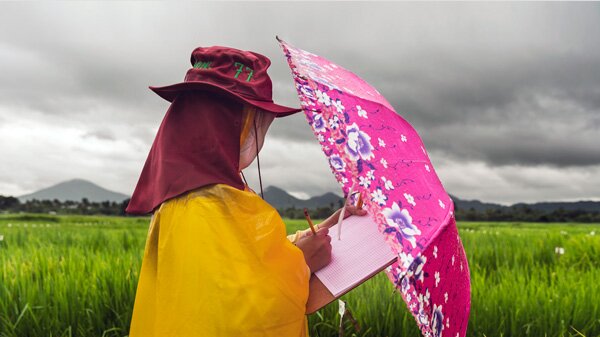 Person in field with umbrella and clipboard