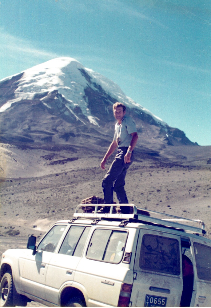 Dr. Debouck standing on the roof of a parked car in front of a mountain.